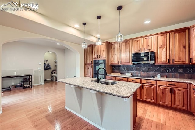 kitchen with a center island with sink, light hardwood / wood-style flooring, sink, pendant lighting, and light stone countertops