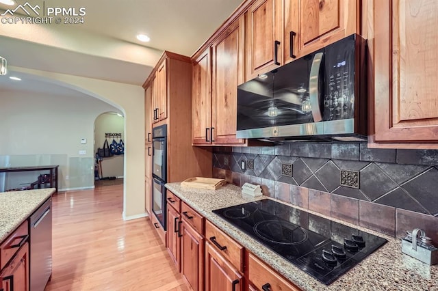 kitchen featuring light hardwood / wood-style floors, light stone counters, tasteful backsplash, and black appliances