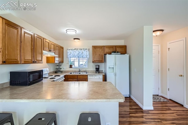 kitchen featuring a breakfast bar, sink, dark hardwood / wood-style flooring, kitchen peninsula, and white appliances