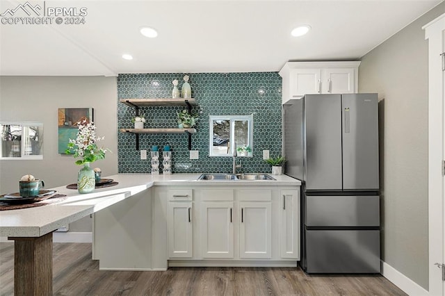 kitchen featuring decorative backsplash, stainless steel fridge, light wood-type flooring, sink, and white cabinets