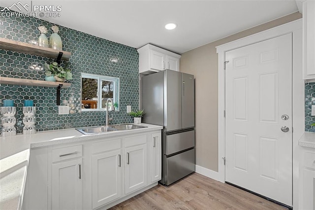 kitchen with sink, light hardwood / wood-style flooring, decorative backsplash, stainless steel fridge, and white cabinetry