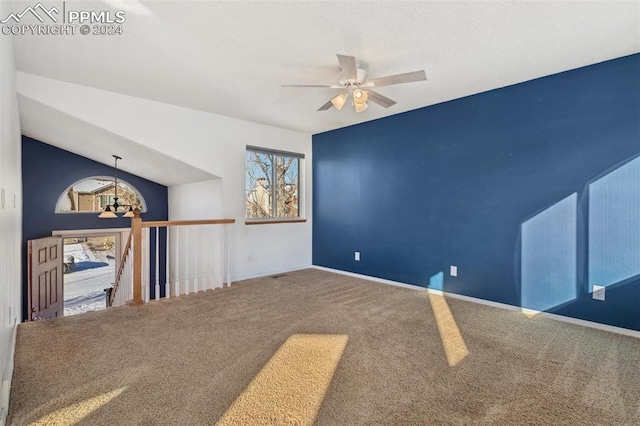 carpeted spare room featuring ceiling fan with notable chandelier and lofted ceiling