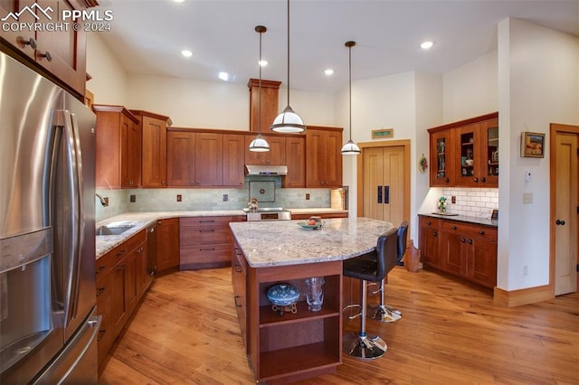 kitchen featuring a center island, hanging light fixtures, stainless steel appliances, light stone counters, and light hardwood / wood-style floors