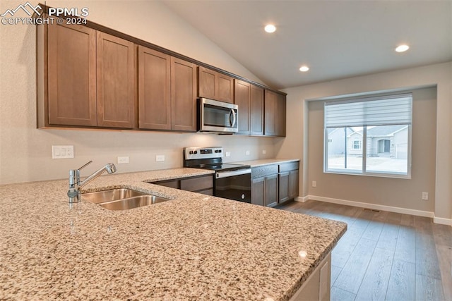 kitchen featuring appliances with stainless steel finishes, vaulted ceiling, light stone counters, and sink