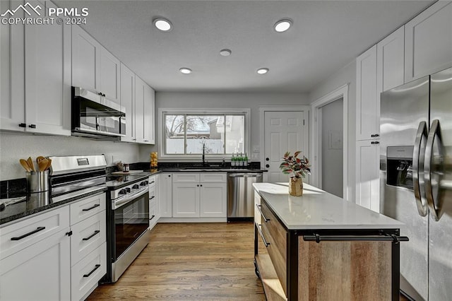 kitchen with sink, dark stone countertops, light hardwood / wood-style floors, white cabinetry, and stainless steel appliances