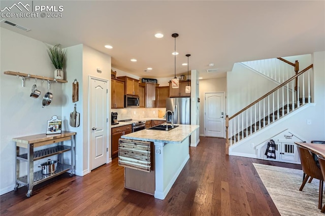 kitchen with dark hardwood / wood-style flooring, stainless steel appliances, sink, pendant lighting, and an island with sink