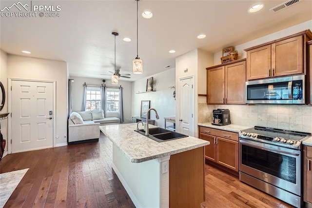 kitchen with appliances with stainless steel finishes, dark hardwood / wood-style flooring, sink, hanging light fixtures, and an island with sink