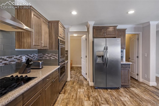 kitchen with crown molding, stainless steel appliances, light stone countertops, and wall chimney range hood