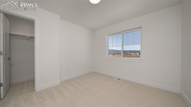 unfurnished bedroom featuring baseboards, a closet, light carpet, a walk in closet, and visible vents