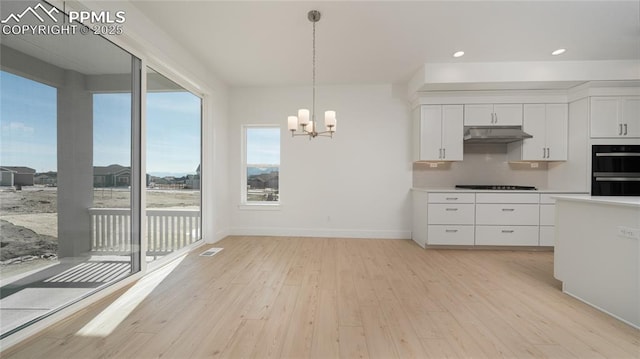 kitchen featuring a chandelier, under cabinet range hood, light wood finished floors, and black appliances
