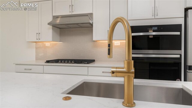 kitchen with white cabinets, under cabinet range hood, backsplash, gas cooktop, and stainless steel double oven