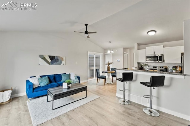 living room featuring ceiling fan with notable chandelier, light wood-type flooring, and vaulted ceiling