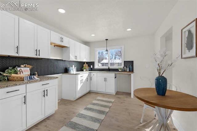 kitchen with light stone countertops, backsplash, light hardwood / wood-style flooring, white cabinets, and hanging light fixtures