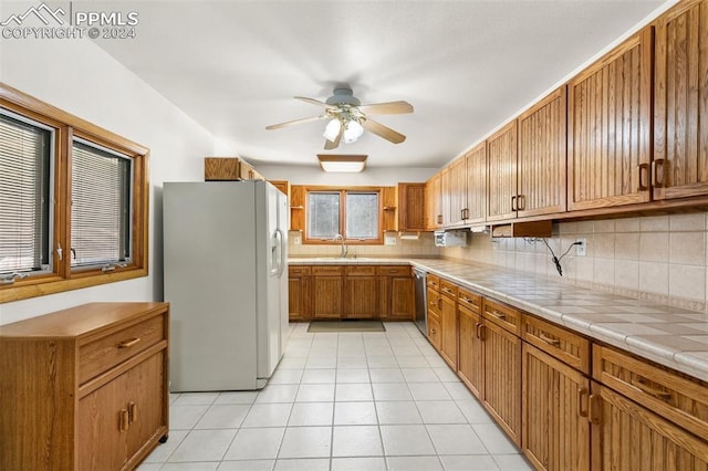 kitchen with ceiling fan, white fridge with ice dispenser, stainless steel dishwasher, decorative backsplash, and light tile patterned floors