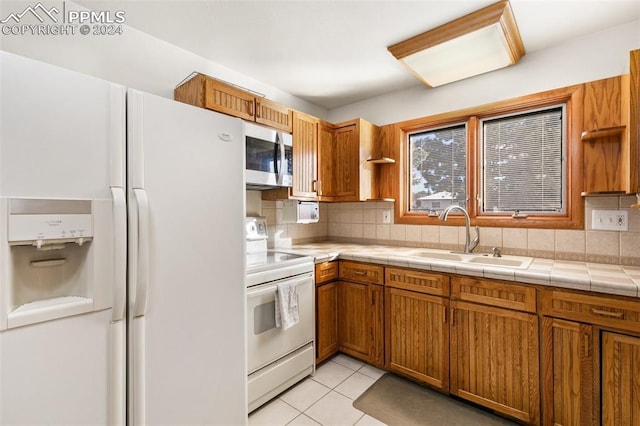 kitchen with tasteful backsplash, white appliances, sink, light tile patterned floors, and tile countertops