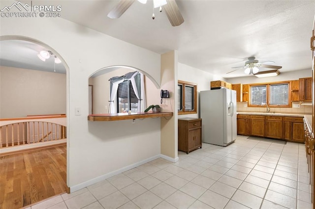 kitchen featuring white refrigerator with ice dispenser, sink, ceiling fan, light tile patterned floors, and tasteful backsplash