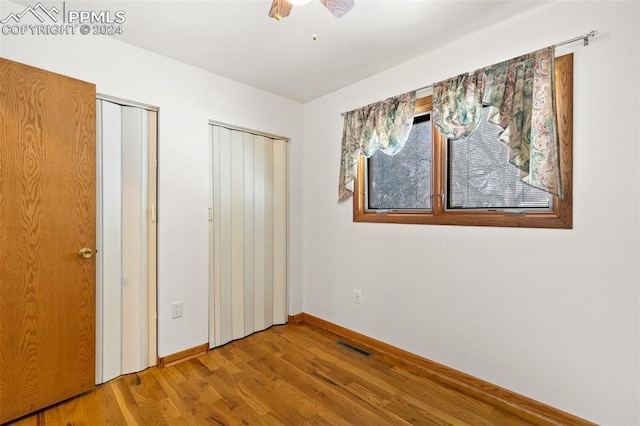 unfurnished bedroom featuring multiple closets, ceiling fan, and wood-type flooring