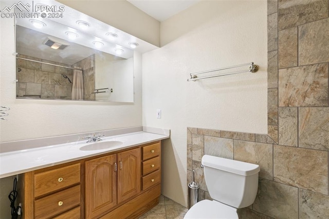 bathroom featuring walk in shower, tile patterned floors, toilet, vanity, and tile walls