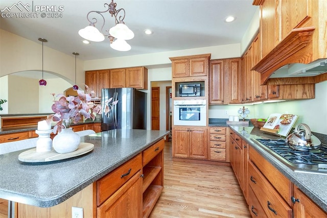 kitchen featuring appliances with stainless steel finishes, light wood-type flooring, custom exhaust hood, pendant lighting, and an inviting chandelier