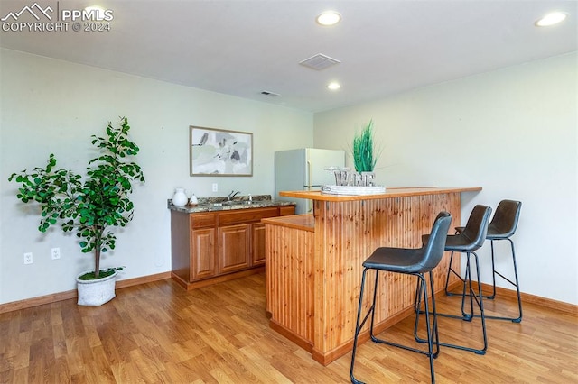 bar featuring light wood-type flooring, white fridge, and sink