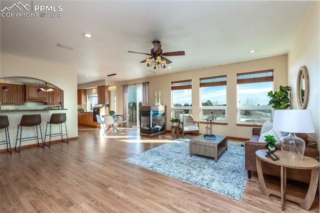 living room featuring ceiling fan, light hardwood / wood-style floors, and a multi sided fireplace