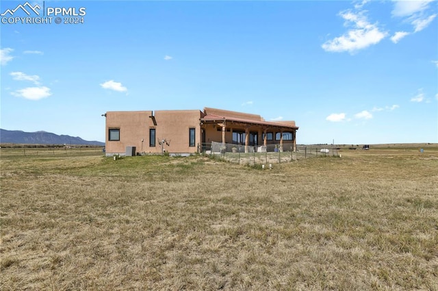 rear view of property with central AC unit, a mountain view, a rural view, and a yard