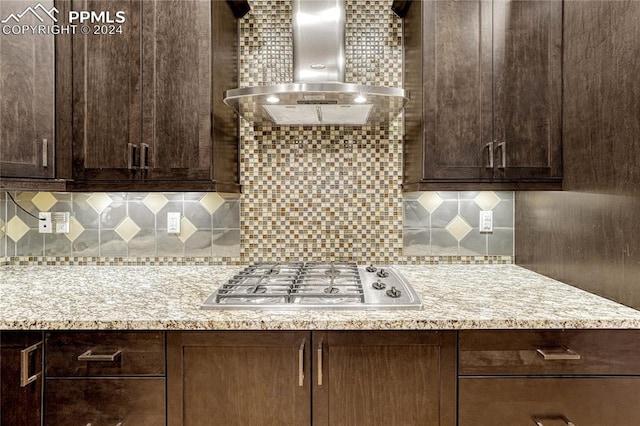 kitchen with tasteful backsplash, light stone counters, wall chimney exhaust hood, and stainless steel gas cooktop