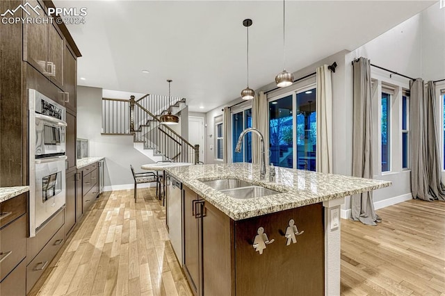 kitchen with decorative light fixtures, light wood-type flooring, an island with sink, and sink