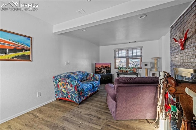 living room featuring beamed ceiling, hardwood / wood-style floors, and a brick fireplace