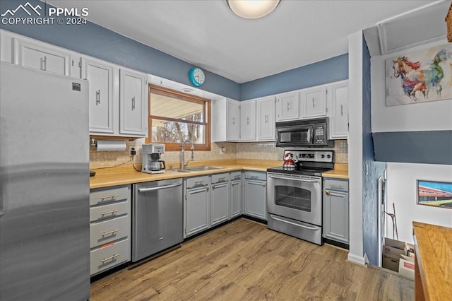 kitchen with decorative backsplash, sink, light wood-type flooring, and stainless steel appliances