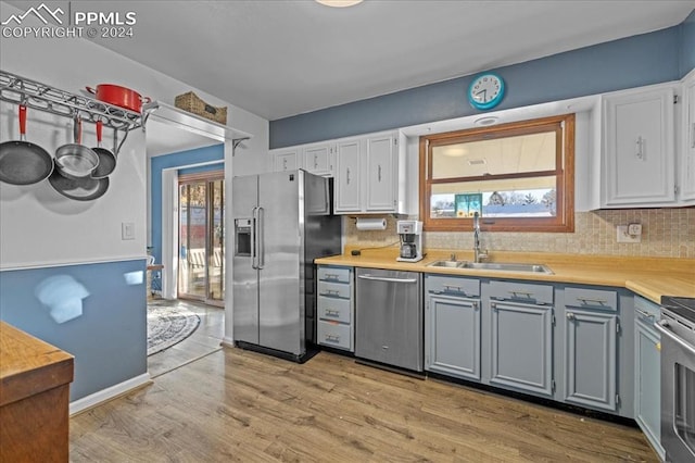 kitchen with white cabinets, sink, appliances with stainless steel finishes, tasteful backsplash, and light hardwood / wood-style floors