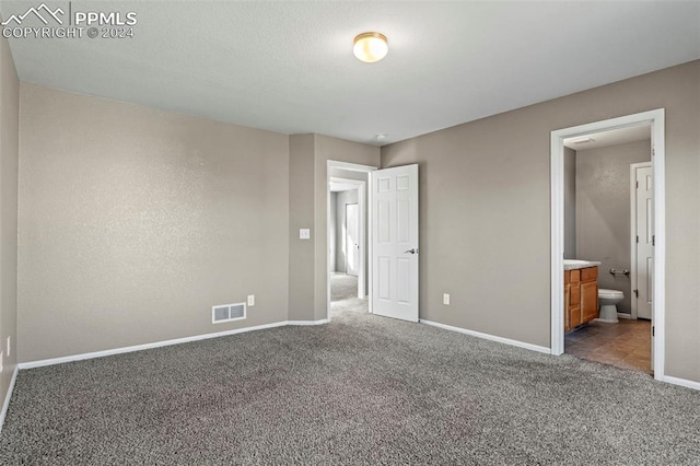 unfurnished bedroom featuring ensuite bathroom and dark colored carpet