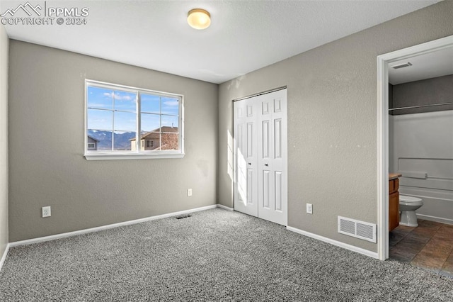 unfurnished bedroom featuring ensuite bathroom, dark carpet, and a closet