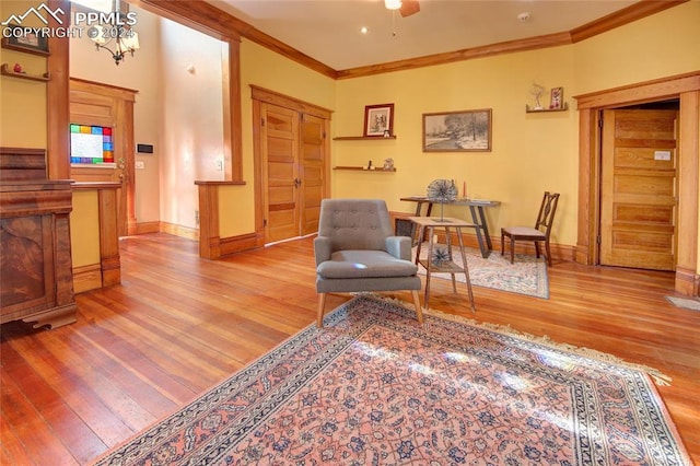 living area with crown molding, ceiling fan with notable chandelier, and light wood-type flooring