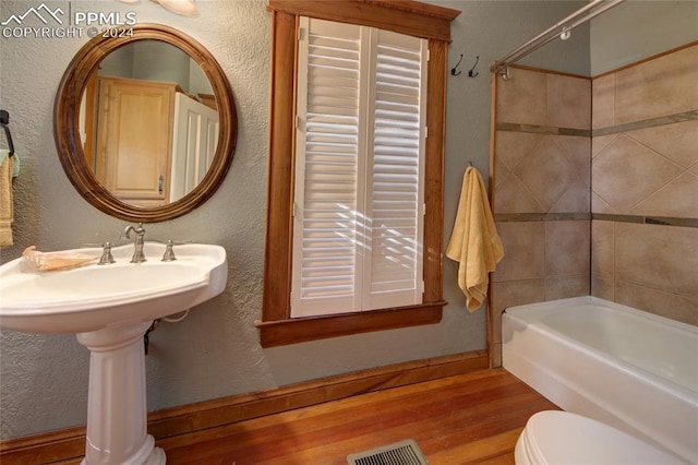 bathroom with hardwood / wood-style floors, tiled shower / bath combo, and toilet