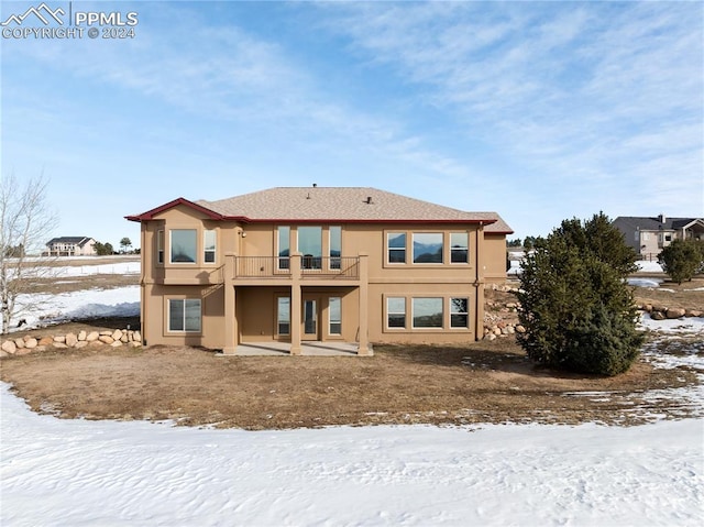 snow covered back of property with a balcony