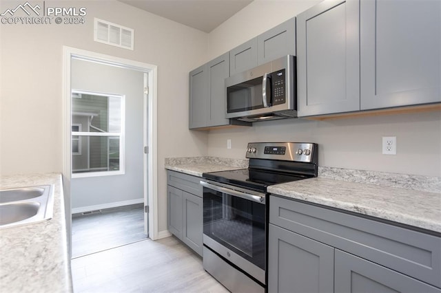 kitchen with gray cabinets, sink, light wood-type flooring, and stainless steel appliances