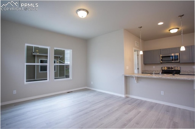 kitchen featuring hanging light fixtures, gray cabinets, light stone countertops, appliances with stainless steel finishes, and light hardwood / wood-style floors