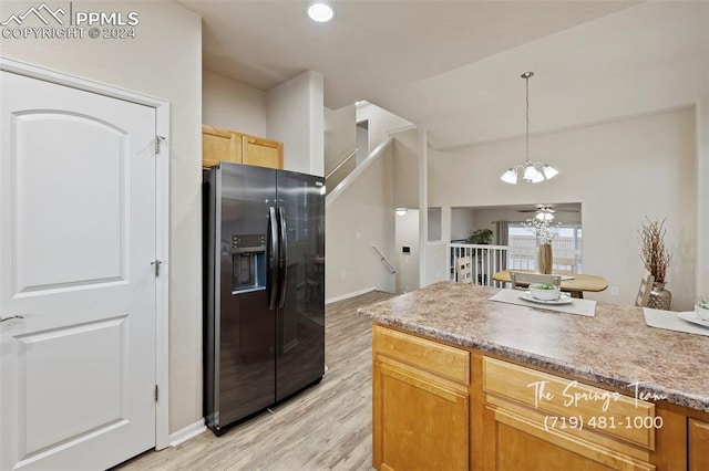 kitchen with stainless steel fridge, pendant lighting, ceiling fan with notable chandelier, and light hardwood / wood-style floors