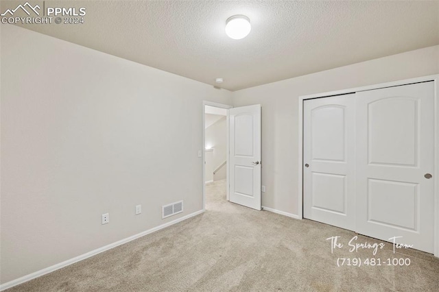 unfurnished bedroom with a textured ceiling, light carpet, and a closet