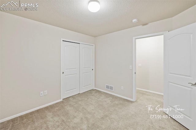 unfurnished bedroom with a closet, light colored carpet, and a textured ceiling