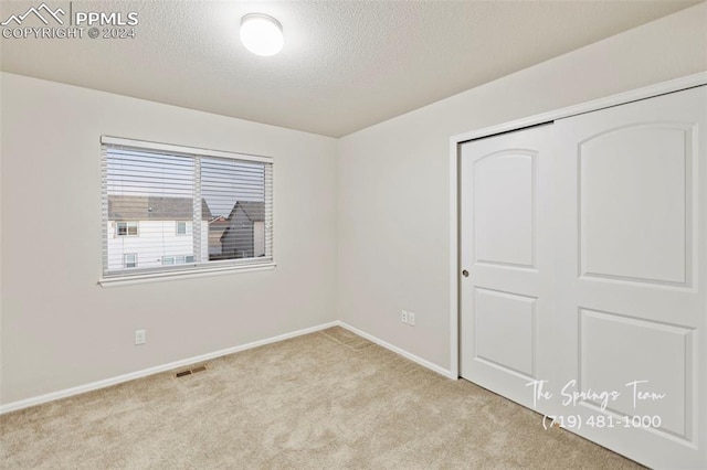 unfurnished bedroom with a closet, light colored carpet, and a textured ceiling