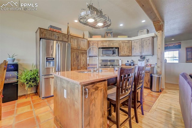 kitchen featuring a kitchen breakfast bar, light stone counters, an island with sink, light hardwood / wood-style floors, and appliances with stainless steel finishes