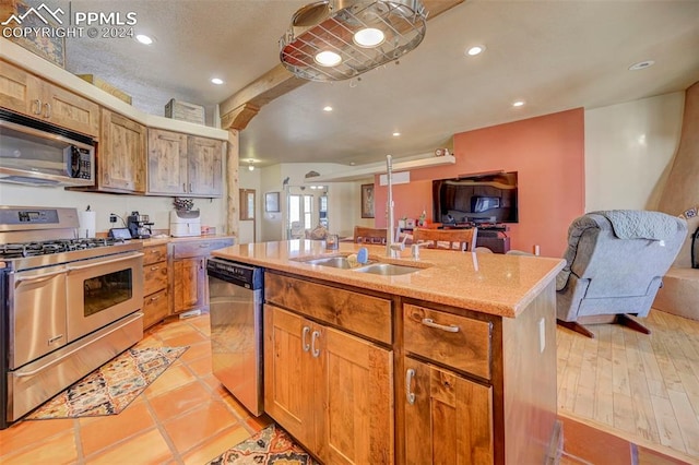 kitchen with sink, light stone counters, light hardwood / wood-style flooring, an island with sink, and appliances with stainless steel finishes