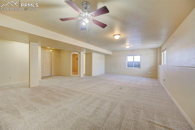 basement featuring a textured ceiling, light colored carpet, and ceiling fan