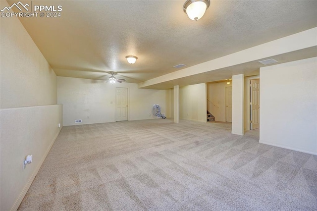 basement featuring a textured ceiling, light colored carpet, and ceiling fan