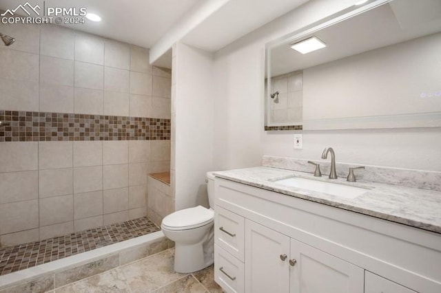 bathroom with tiled shower, vanity, and toilet