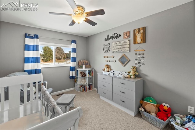 bedroom with light colored carpet, a nursery area, and ceiling fan