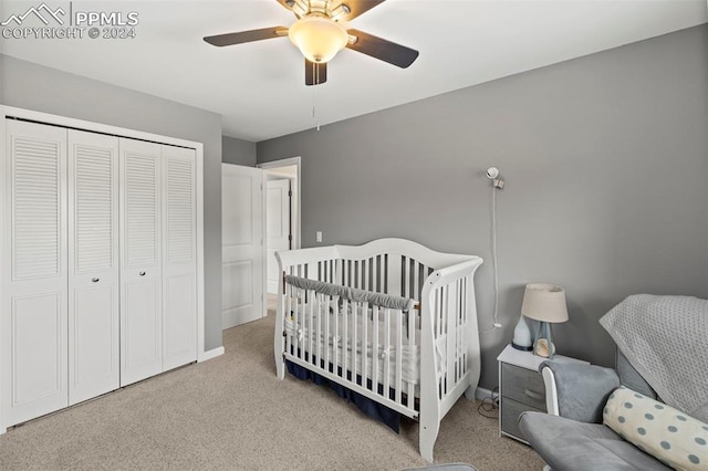 bedroom featuring a crib, a closet, light colored carpet, and ceiling fan