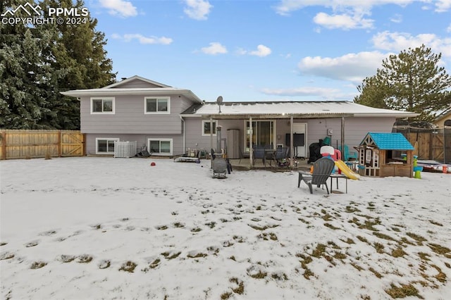 snow covered back of property with a playground